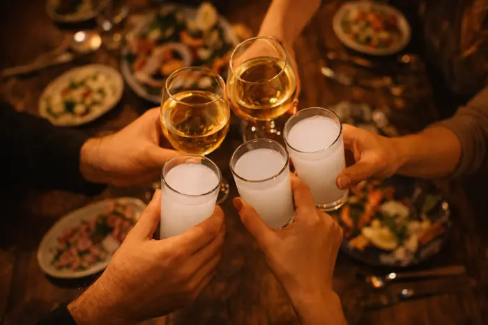 Four hands raising glasses of rakı over a table of meze